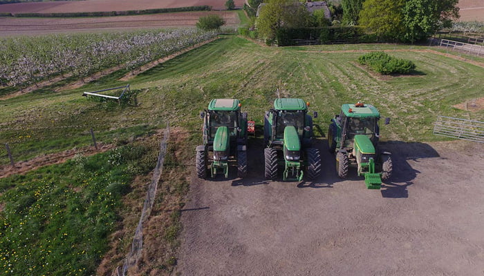 An arial shot of 3 tractors parked at the edge of a farm